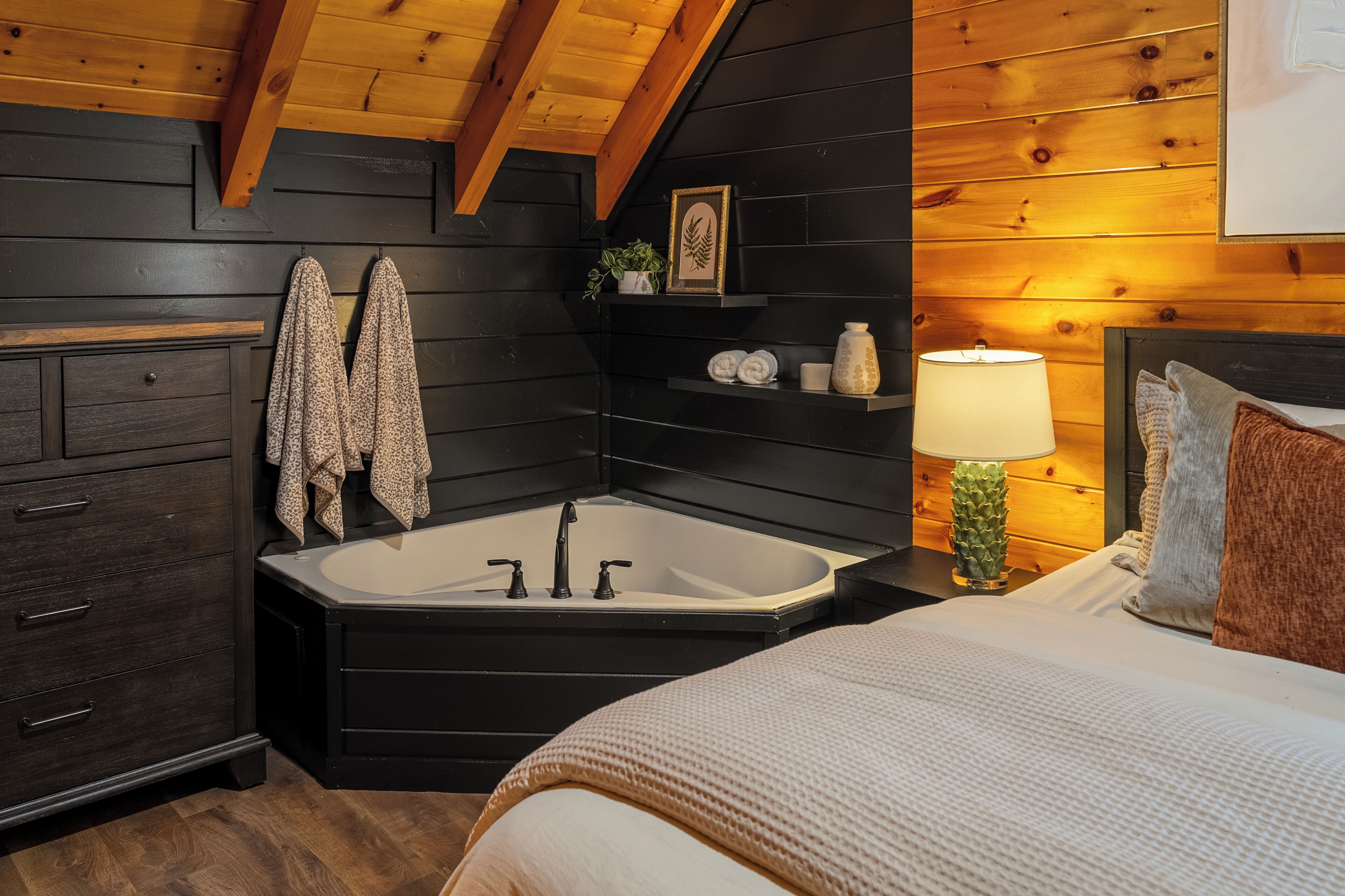 Ein modernes Badezimmer mit freistehender Badewanne, dunklen Holzschränken, einem Handtuchhalter, einem Ablagefach mit Pflegeprodukten und einer Nachttischlampe.