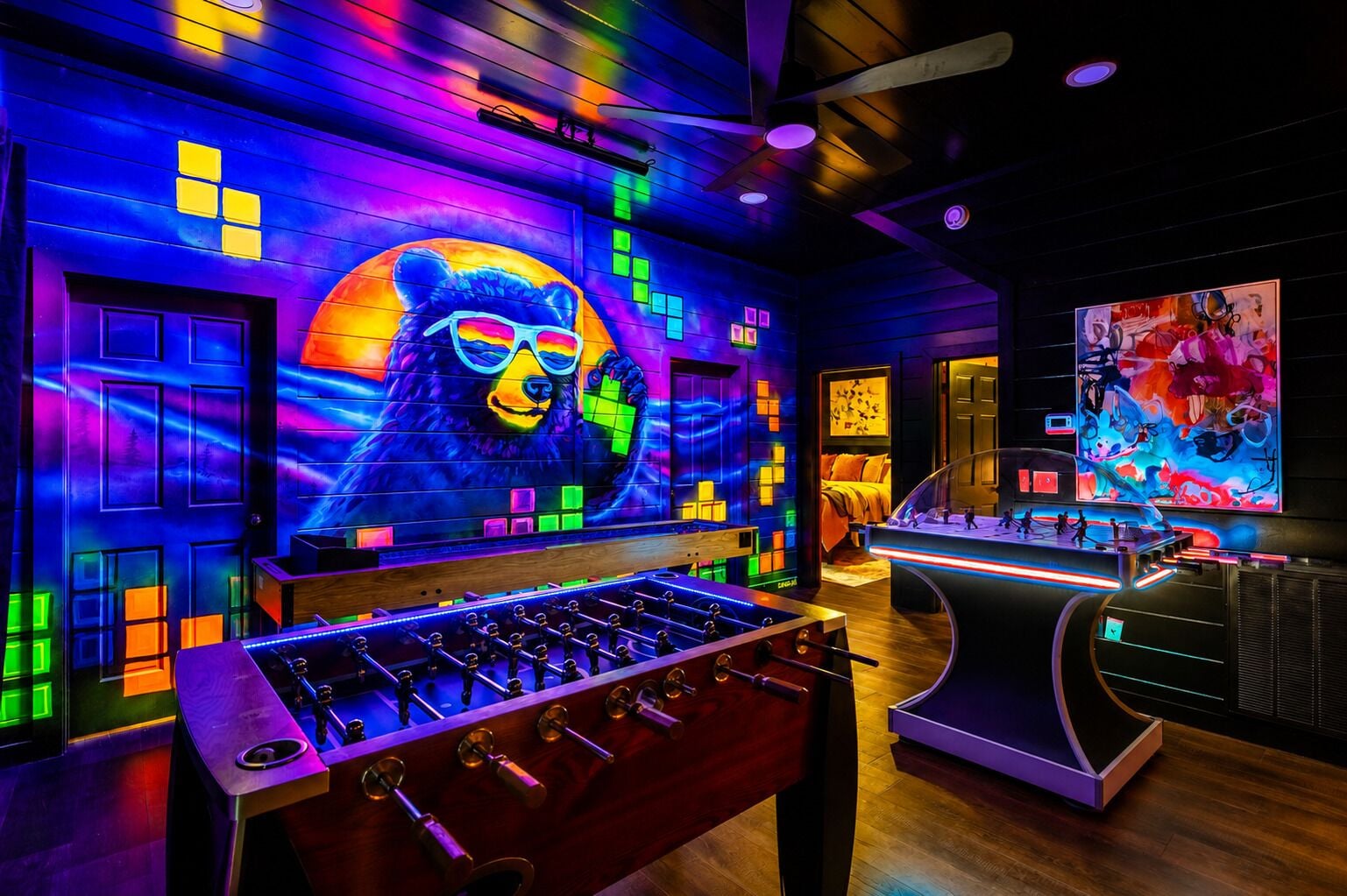 A room with a foosball table, a large bear mural, and a colorful abstract painting.