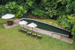Ein Schwimmbecken mit einer umlaufenden Terrasse, inklusive Stühle und Sonnenschirme.