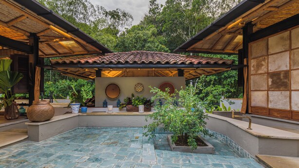 A covered outdoor area with a tiled floor, potted plants, and a wall with decorative plates.
