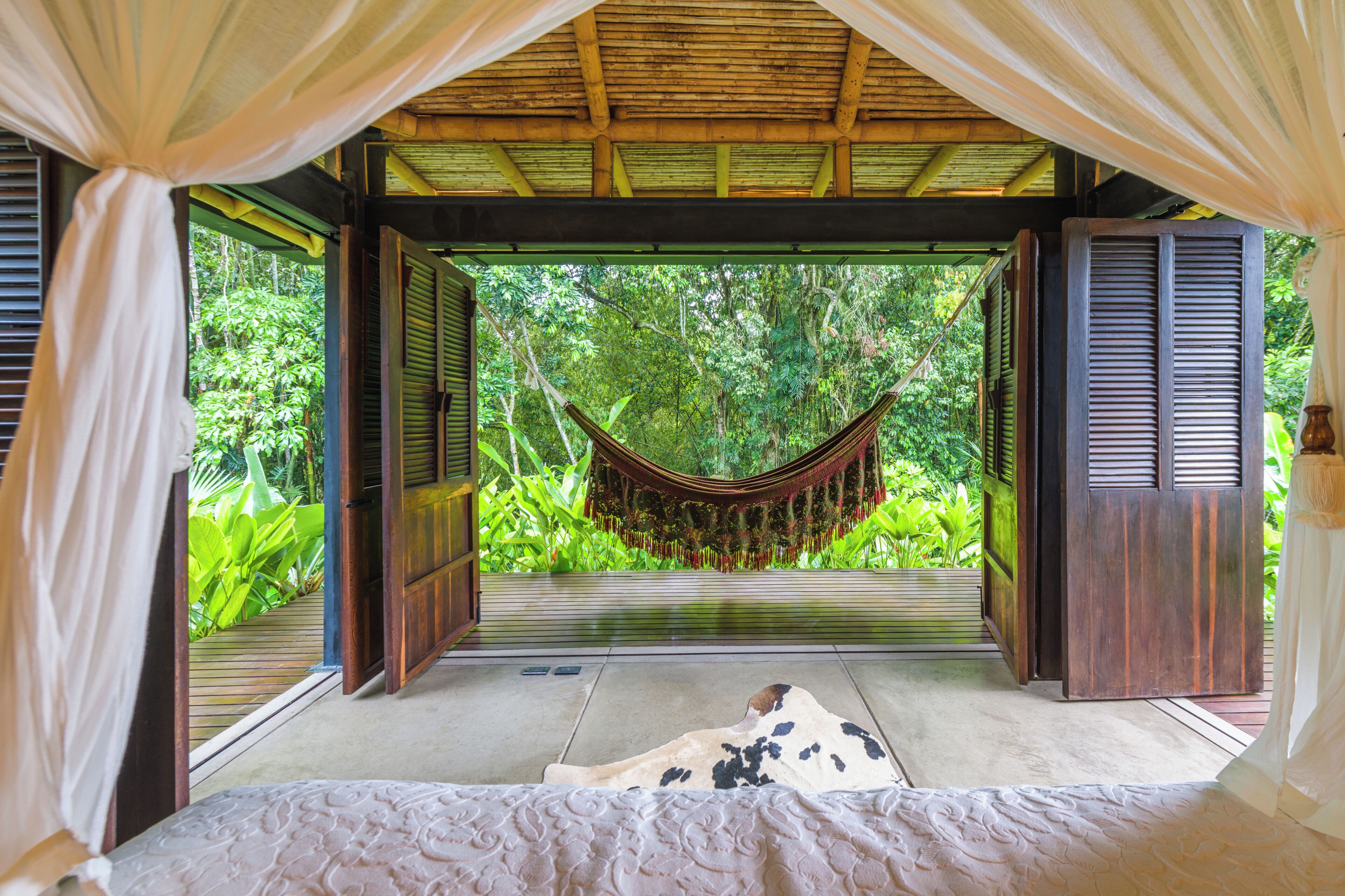 A room with a bed, a hammock, and a view of lush greenery.