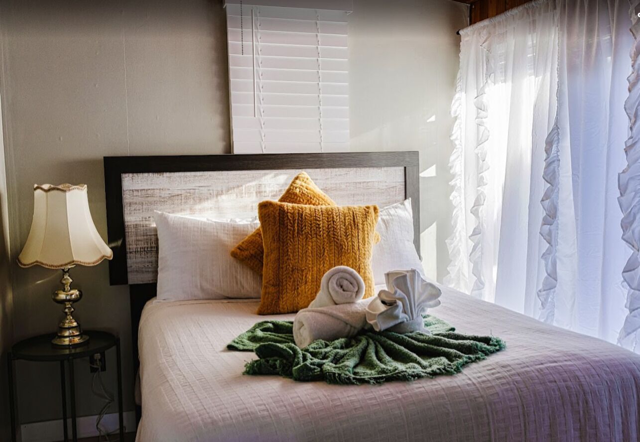 A neatly made bed with a star-shaped pillow, a rolled towel, and a green blanket.