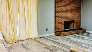 Un salon avec une cheminée en briques, un plancher en bois et un rideau jaune.