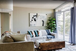 A living room with a sofa, a coffee table, a painting, and a plant.