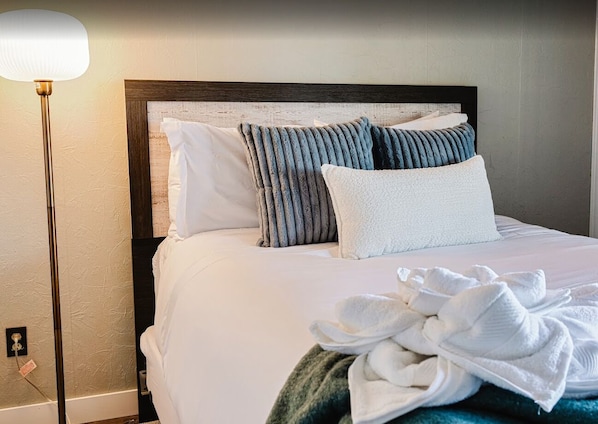 A neatly made bed with white linens, a dark wooden headboard, and a pile of white towels on the bed.