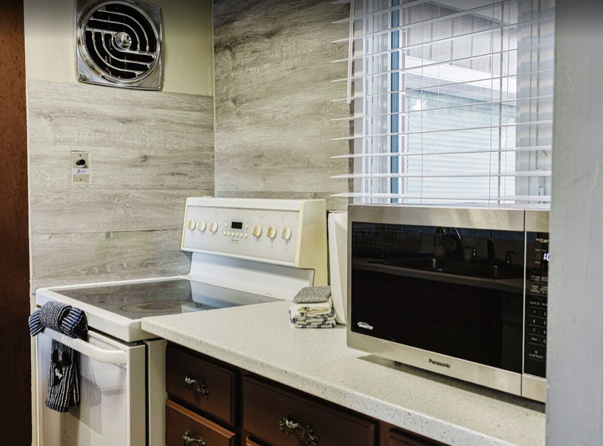 Una cocina con estufa, microondas y ventana con persianas.
