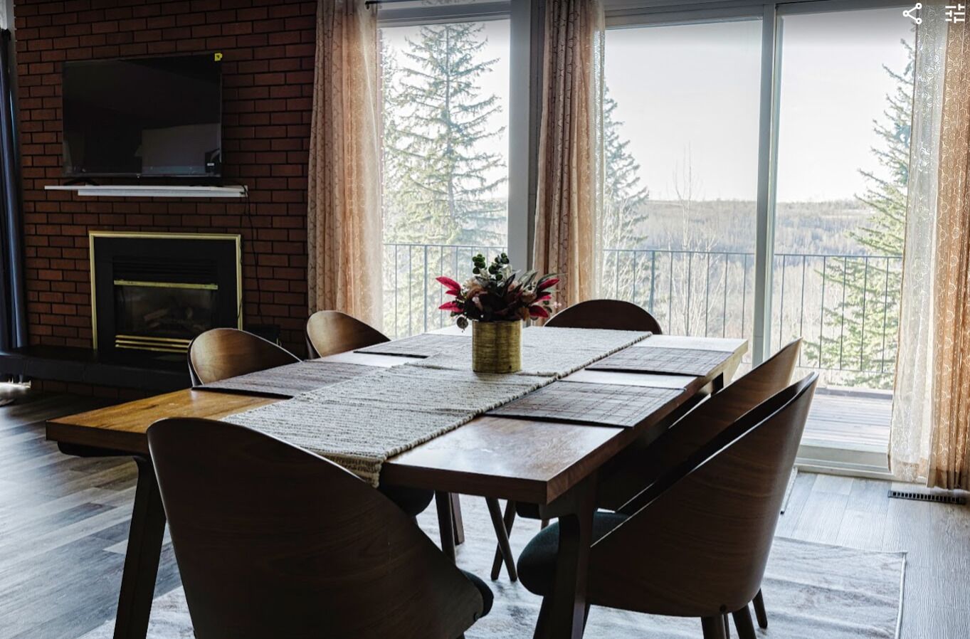 A dining area with a brick fireplace, a TV mounted above it, and a table set for six with chairs.