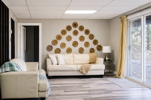 Un salón con sofá, una silla pequeña, una lámpara y un panel decorado con objetos trenzados circulares.