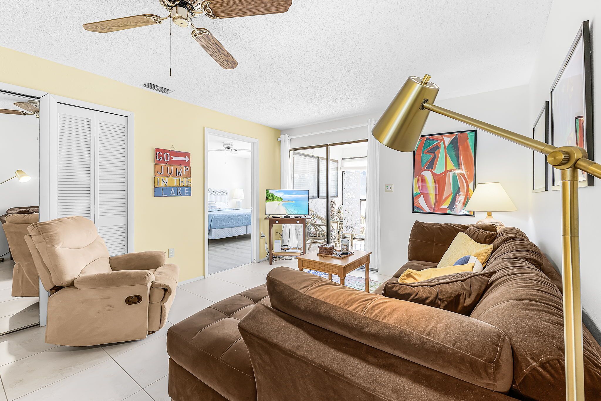 A living room with a recliner, a sofa, a television, a ceiling fan, and a painting on the wall.