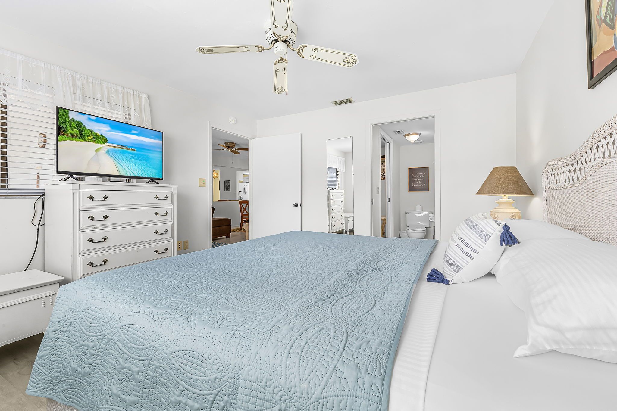 Une chambre avec un lit, une télévision, un ventilateur de plafond et une vue sur la plage.