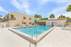 Ein Schwimmbecken mit Metallgeländer, ein überdachter Bereich mit einer Tür und ein Gebäude mit beige-farbener Fassade und Rundbogenfenstern.