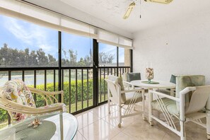 Ein Balkon mit Blick auf einen Tennisplatz und Grünflächen, ausgestattet mit einem Tisch, Stühlen und einer dekorativen Glasvase.