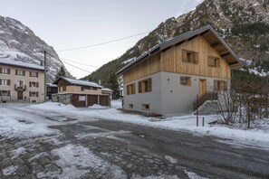 A wooden building with a sloped roof, a stone wall, and a paved road in a snowy mountainous area. - Balcony, tv, 30m², Pralognan-la-Vanoise (Pralognan-la-Vanoise)