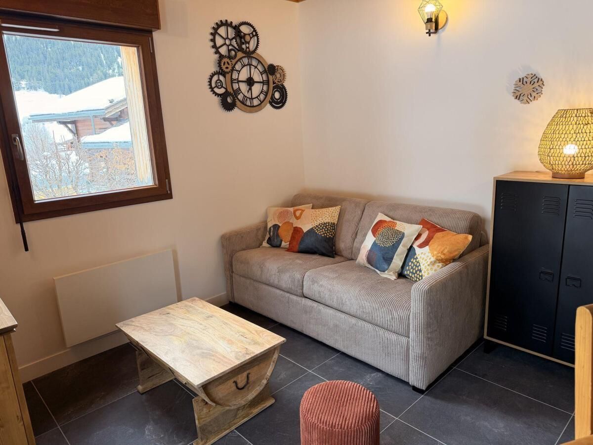 Een gezellige woonkamer met een bank, een houten salontafel, een radiator en een raam met uitzicht op een besneeerd landschap.