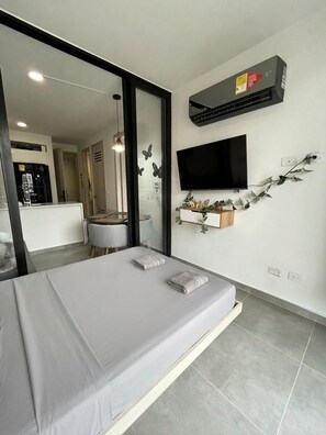 Une chambre moderne équipée d’un lit, d’une télévision, d’un appareil de climatisation et offrant une vue sur la cuisine.