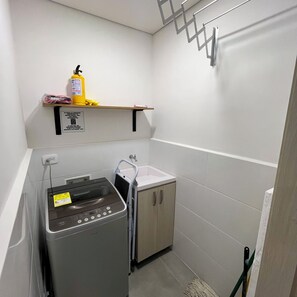 A compact laundry area with a washing machine, a sink, and a shelf with cleaning supplies. - Apartment in Santa Marta | 5-minute drive from the beach (Santa Marta)