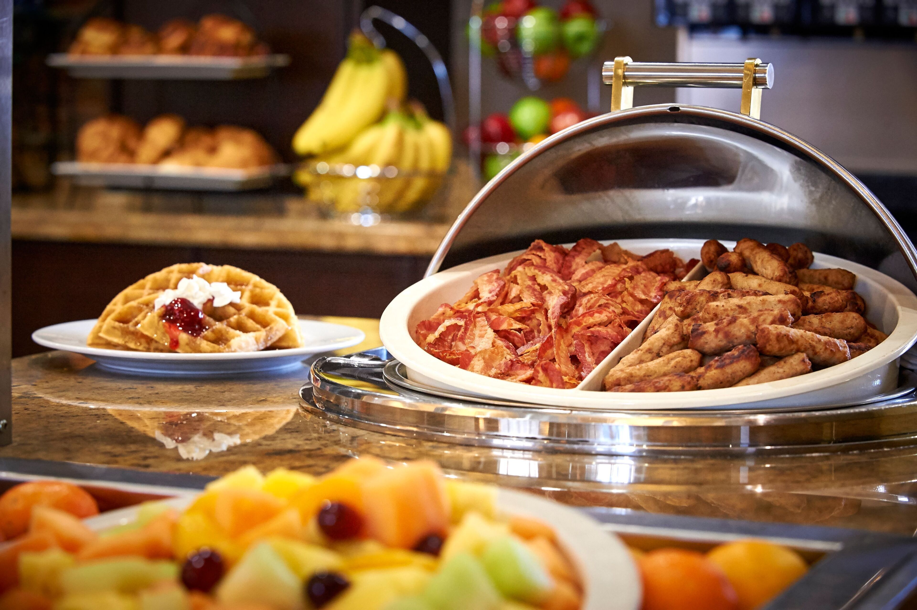 A buffet with various food items including waffles, bacon, and fruit.