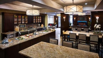 A hotel breakfast area with a buffet, seating, and a bar.