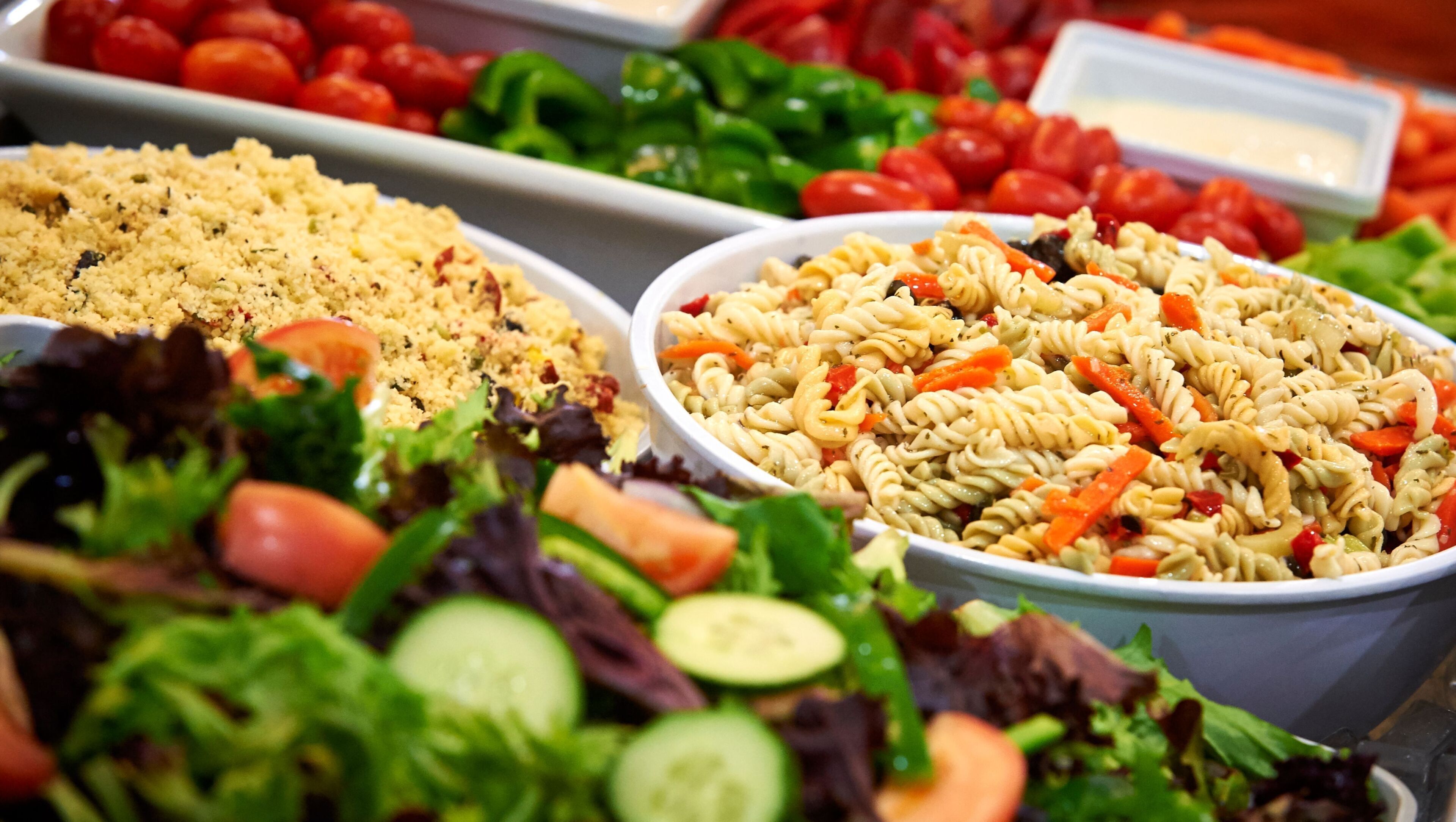 Un buffet proposant divers plats, notamment une salade de pâtes, du couscous et une salade composée de différentes variétés de légumes verts et autres légumes.