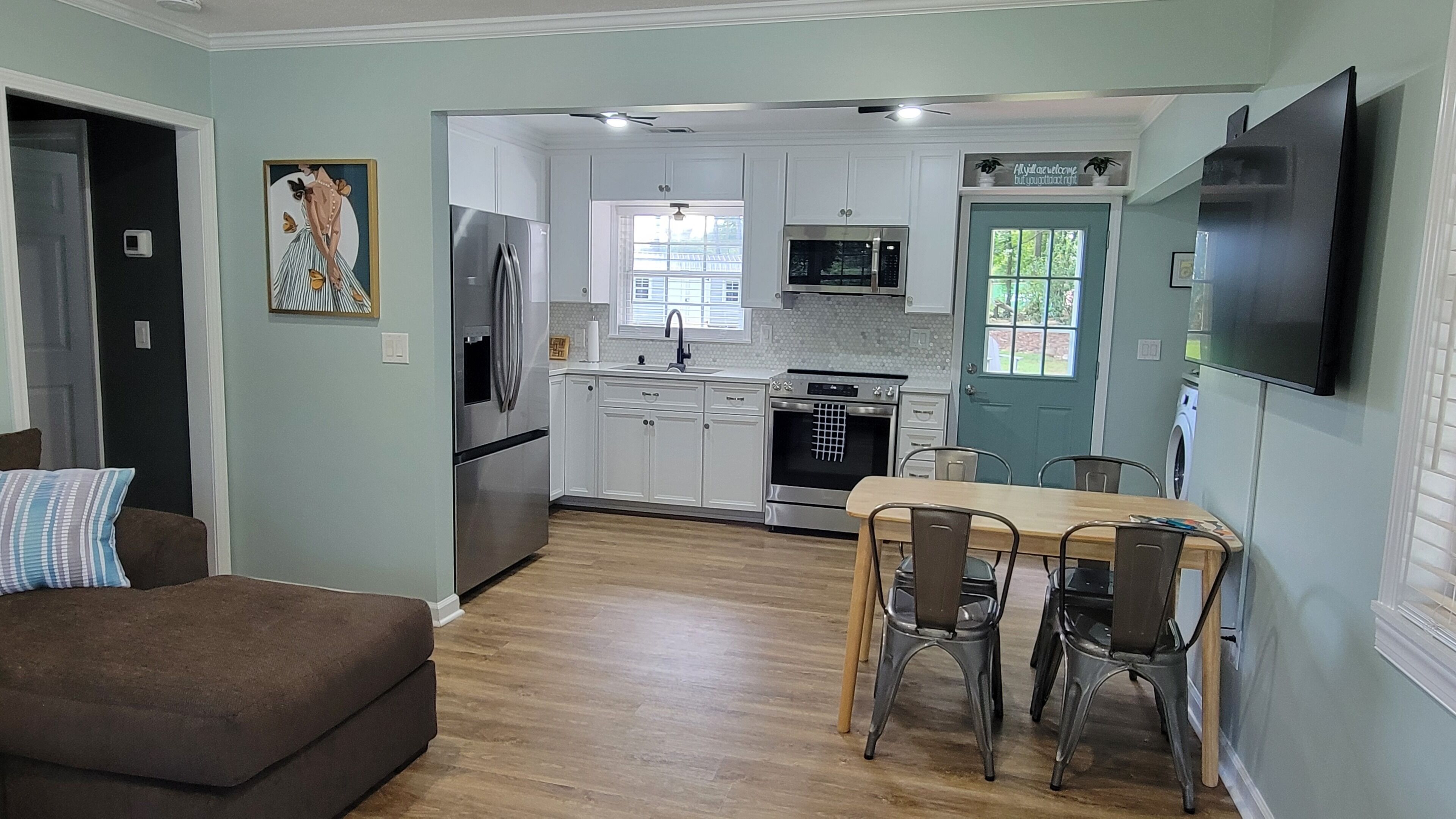 A modern kitchen with white cabinets, stainless steel appliances, and a dining area with a wooden table and metal chairs.