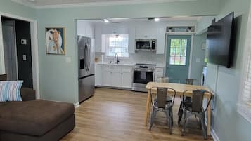 A modern kitchen with white cabinets, stainless steel appliances, and a dining area with a wooden table and metal chairs.