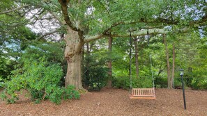 Un ensemble de balançoires en bois installé dans un espace boisé, avec un banc et un lampadaire.