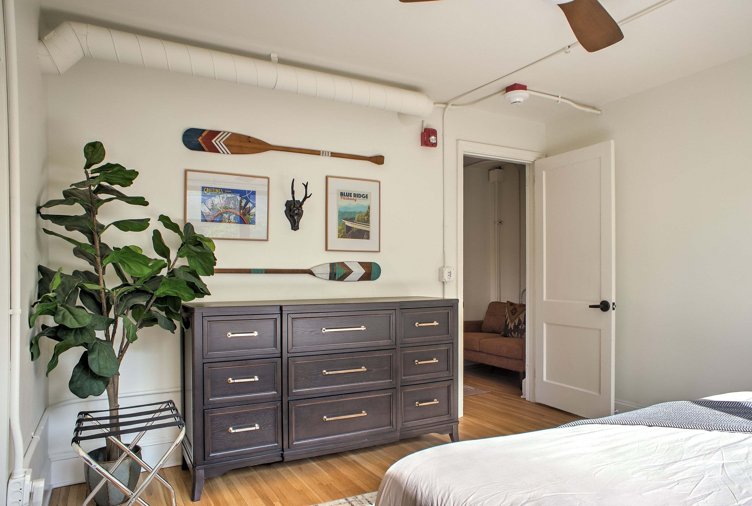 A bedroom with a bed, a dresser, a plant, and wall decorations including a framed picture and a mounted animal head.