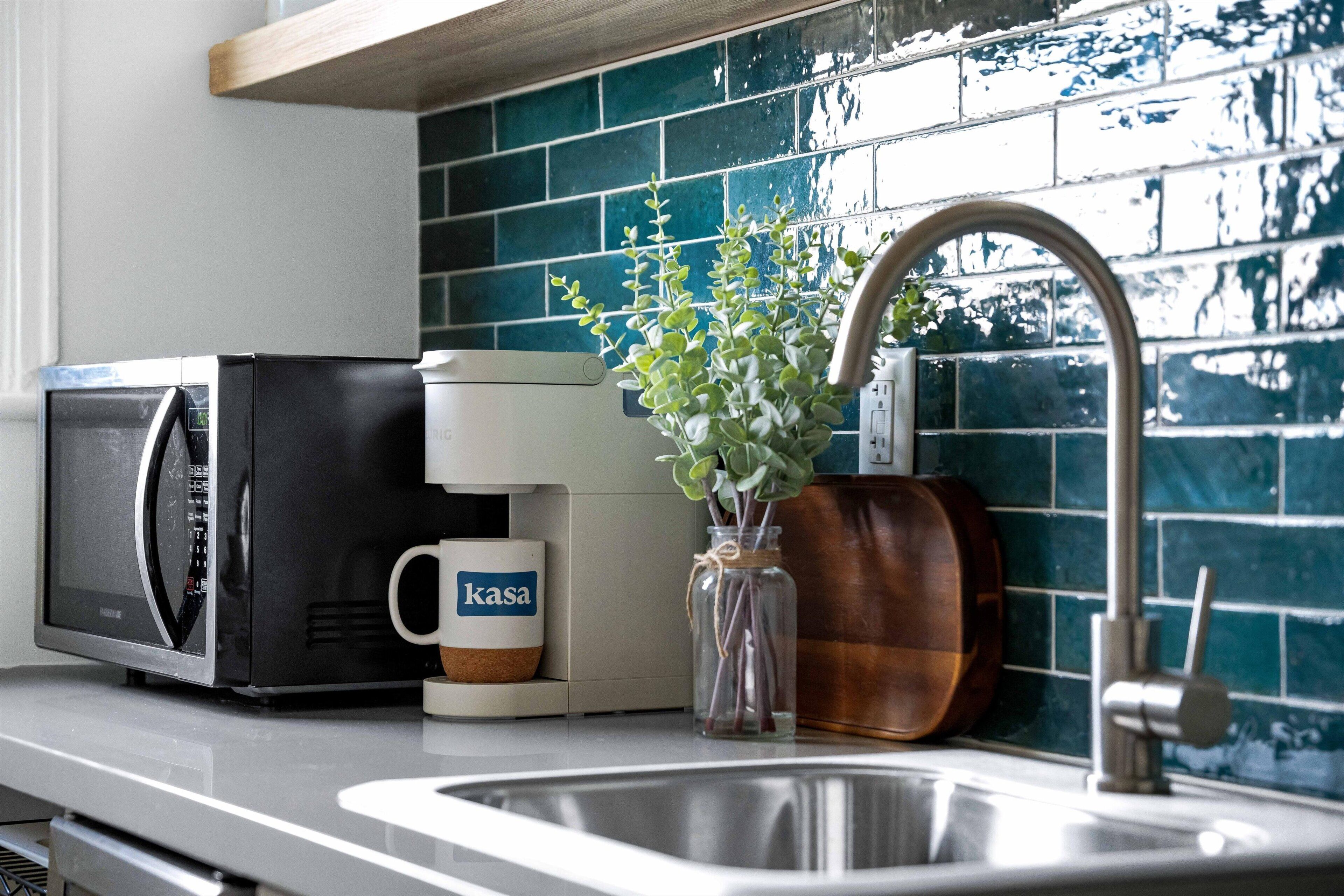 Et køkken med en mikrobølgeovn, kaffemaskine, en vase med grønne planter og en kobberpotte.