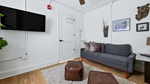 Una sala de estar moderna con televisor de pantalla plana, sofá gris, otomanas marrones y un ventilador de techo.
