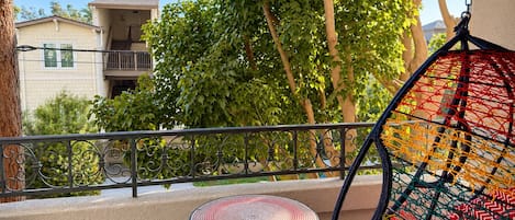 A balcony with a hanging chair, a small round table, and a view of buildings and trees.