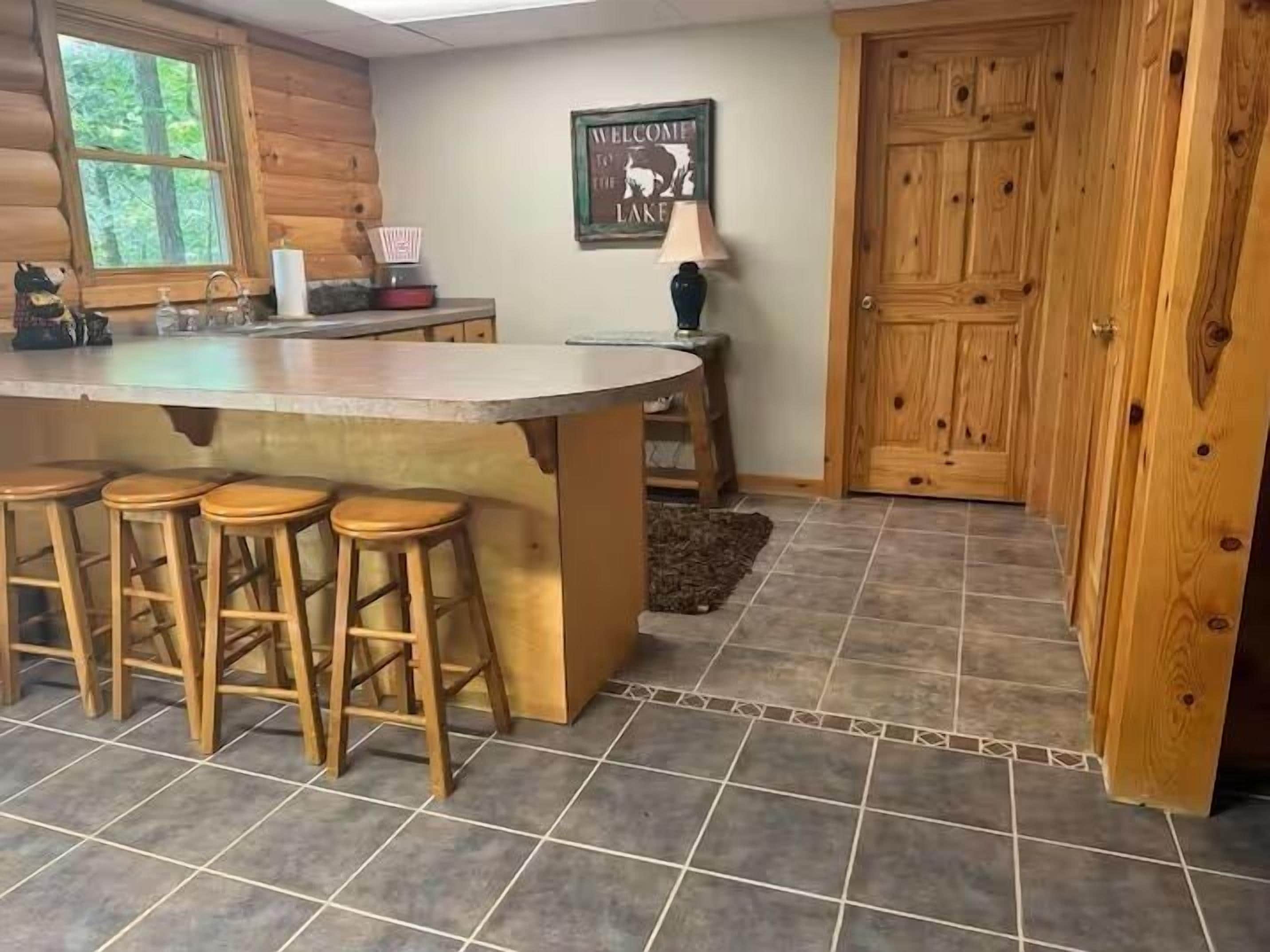 A kitchen with a bar area, wooden stools, a refrigerator, and a door with a sign.