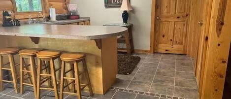 A kitchen with a bar area, wooden stools, a refrigerator, and a door with a sign.