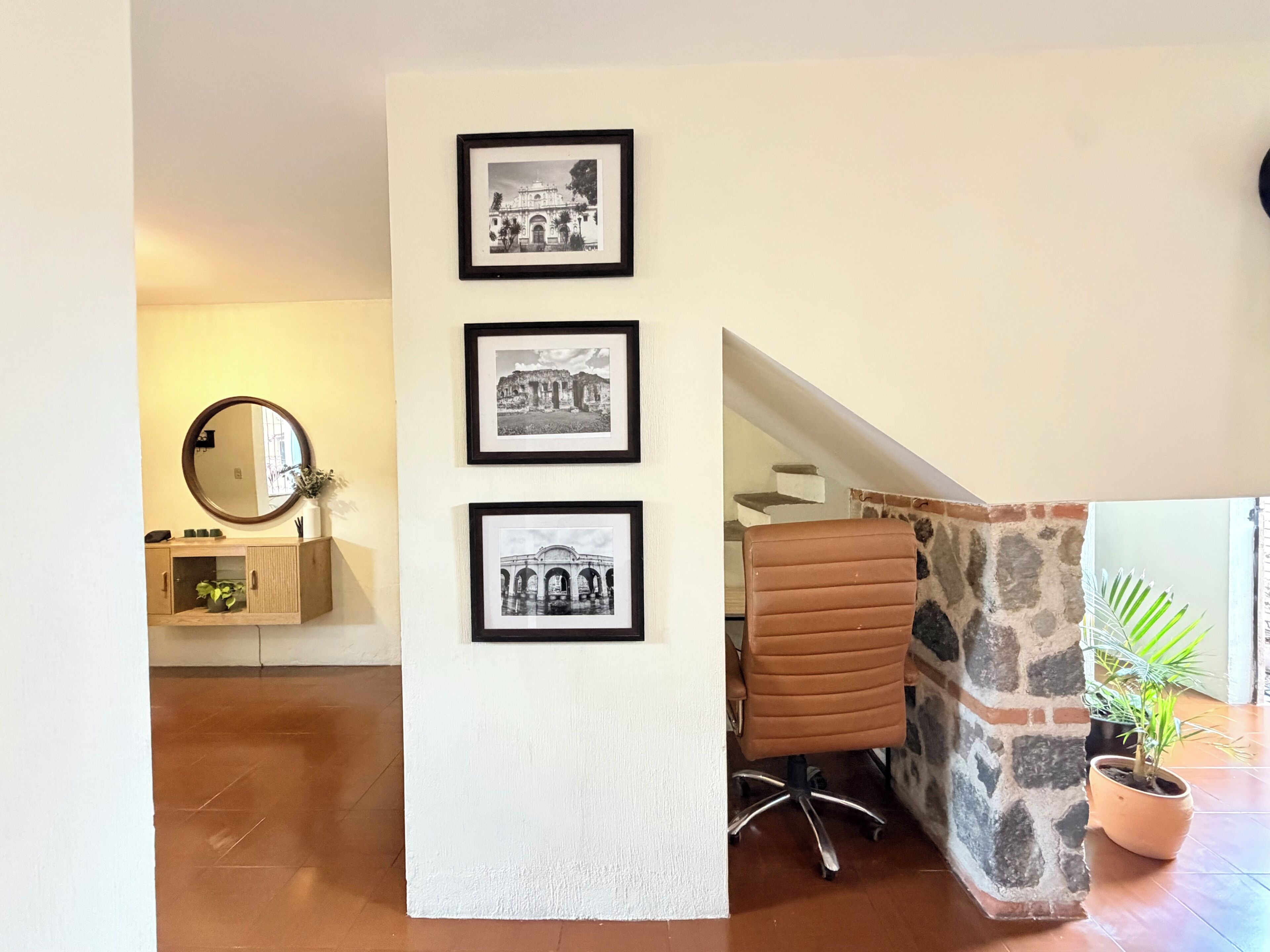 A room with a wooden cabinet, a mirror, a framed black and white photo, a brown leather chair, and a potted plant.