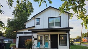 A two-story house with a garage, two windows on the front porch, and a small garden area. - Modern OKC Duplex | Close to OU Med & Downtown (Oklahoma City)