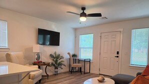 A living room with a sofa, a dining table, a TV mounted on the wall, a ceiling fan, and a door. - Modern OKC Duplex | Close to OU Med & Downtown (Oklahoma City)