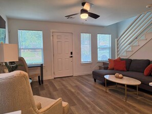 Un salon avec un canapé, une table basse, un fauteuil, une porte et un escalier.