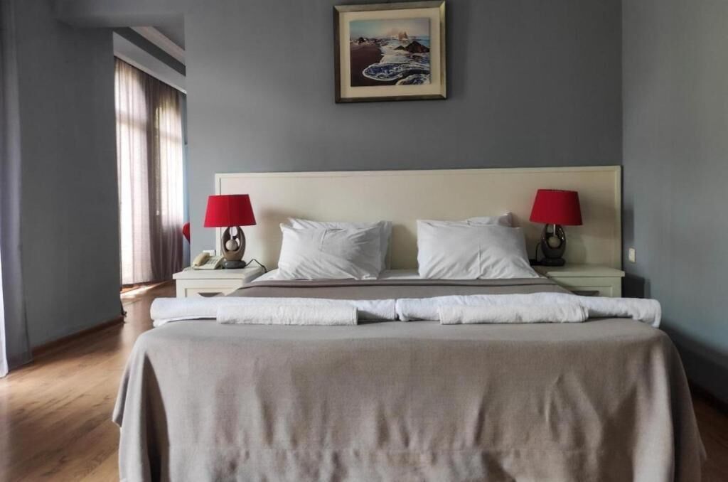 Un dormitorio con cama, dos mesitas de noche, dos lámparas, un cuadro en la pared y una ventana con cortinas.
