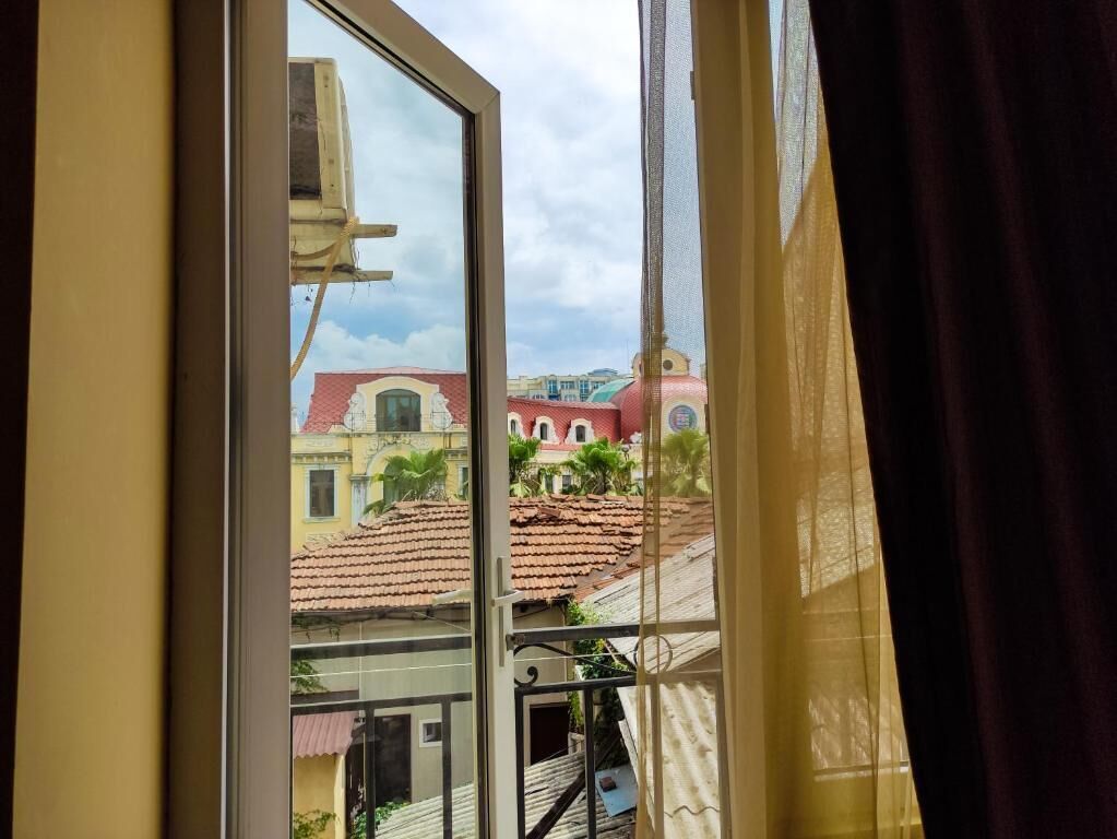 A window with a view of buildings with red roofs and a clear sky.