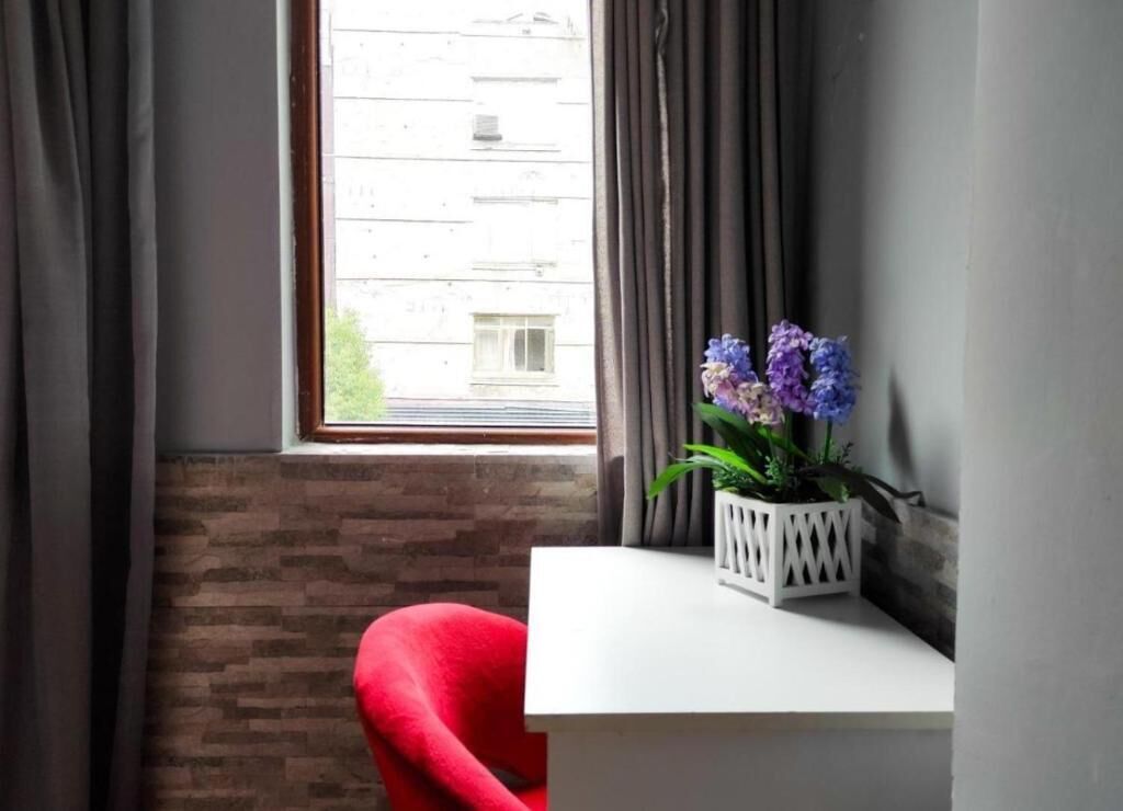 A corner of a room with a white table, a red chair, and a window with curtains.
