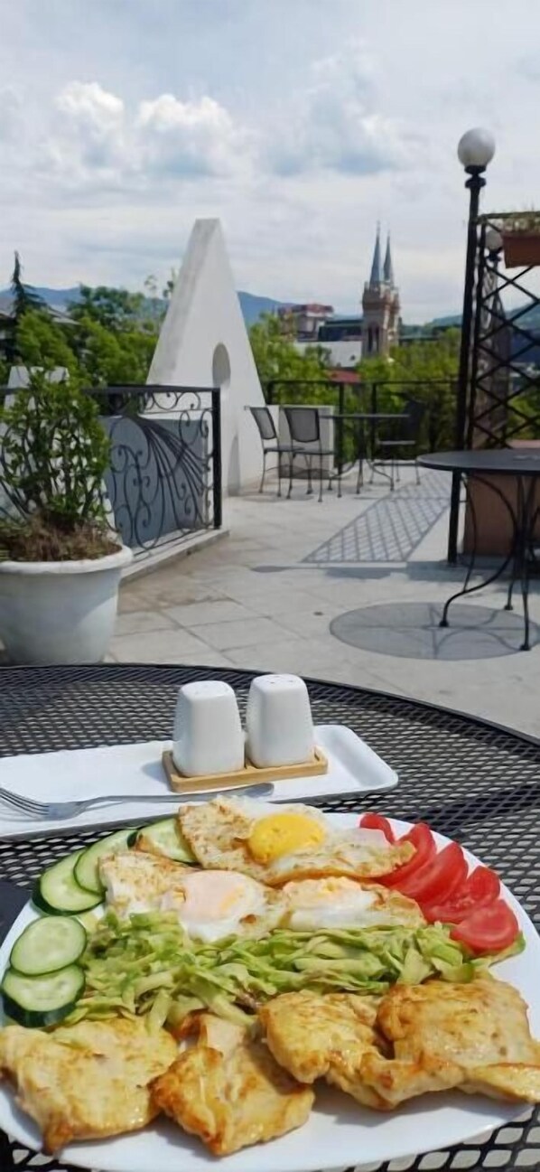 Una mesa de comedor con un plato de comida y dos saleros, frente a un paisaje urbano que incluye una aguja de iglesia al fondo.