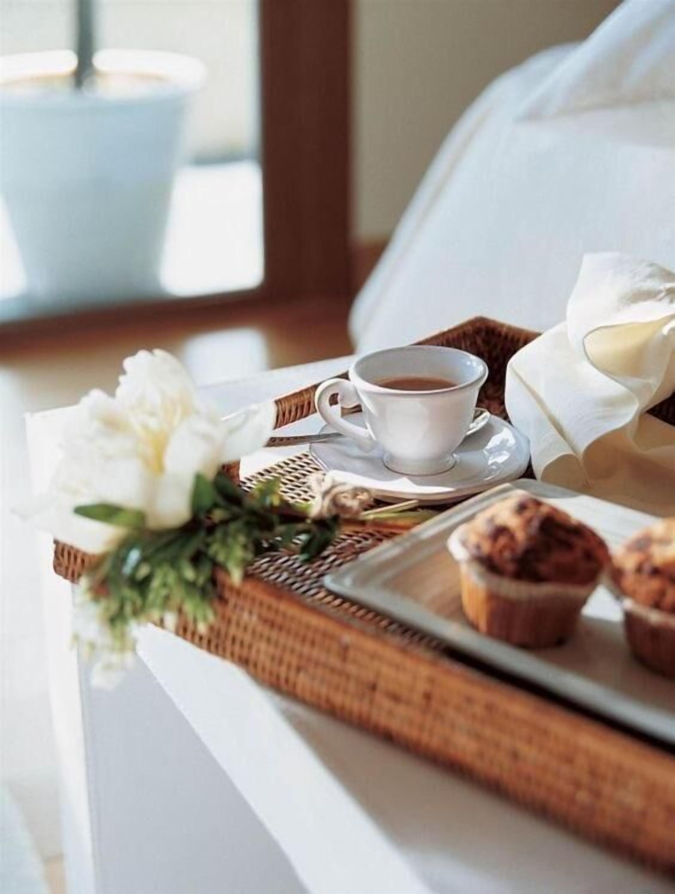A tray with a cup of coffee, muffins, and a white flower on a white table.