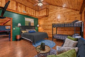 Una cabaña acogedora con una cama litera, una cama individual, una pequeña mesa redonda con un centro de mesa decorativo y una pared verde con un cuadro de paisaje.