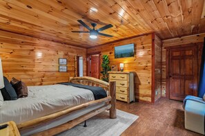 A wooden interior with a bed, a dresser, a ceiling fan, and a painting on the wall. - Gamer’s Den—Drive-In Cinema/Arcade/Outdoor Bowling (Pigeon Forge)