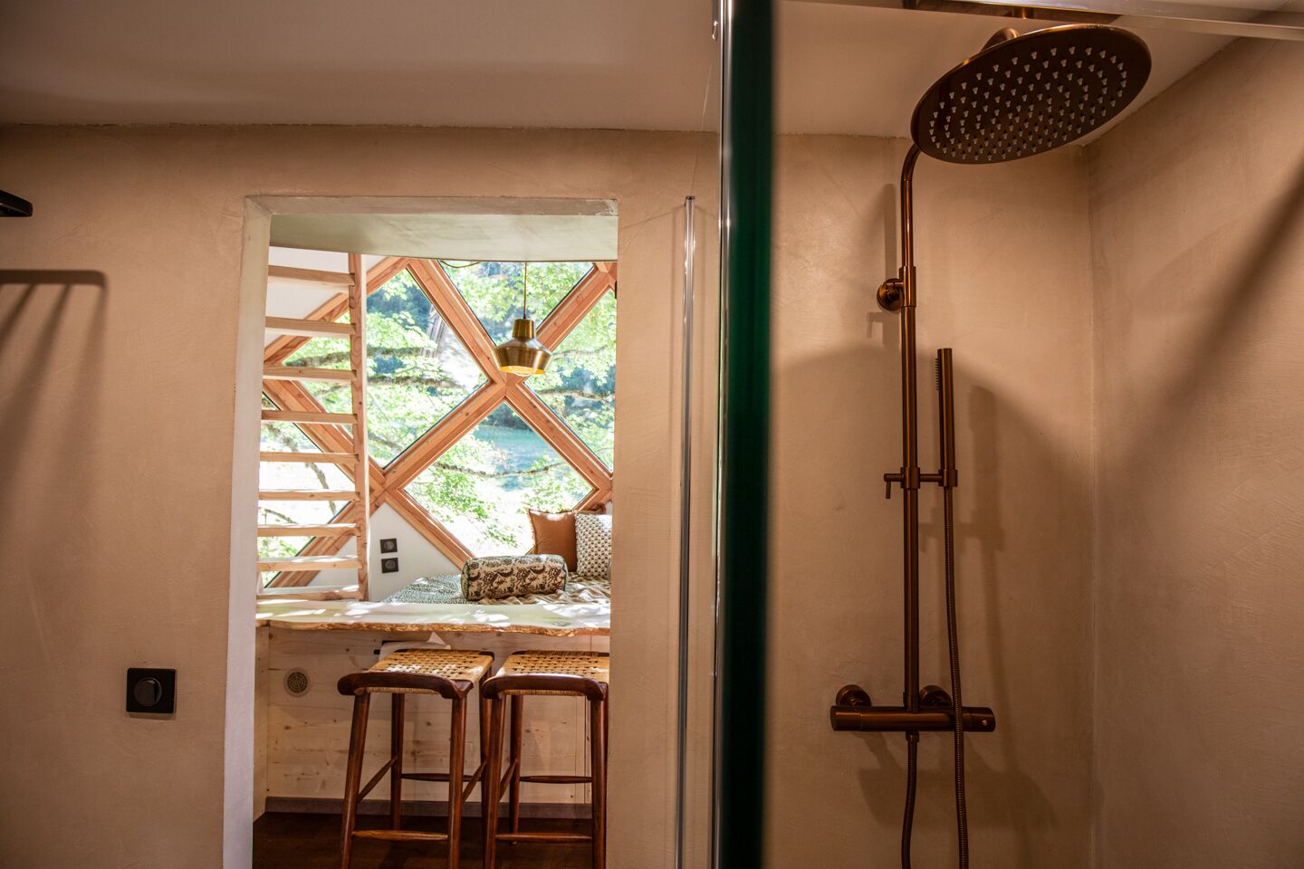Une salle de bain avec une douche, une fenêtre donnant sur un espace verdoyant et un tabouret en bois.