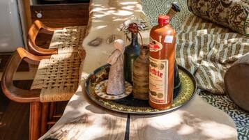 A rustic kitchen with a wooden table, a woven chair, and a bottle of sauce.