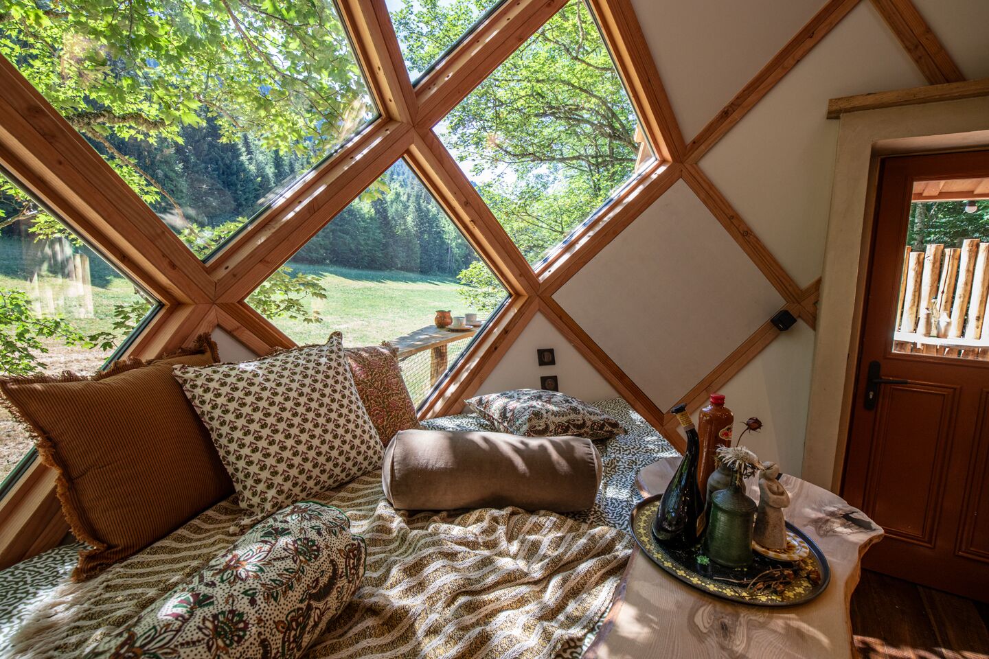 Une pièce confortable avec un lit, des oreillers et une table sur laquelle se trouvent des bouteilles et une tasse.