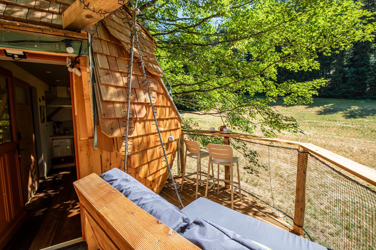 Une cabane en bois dotée d’un balcon, d’un banc et d’une table avec des chaises.