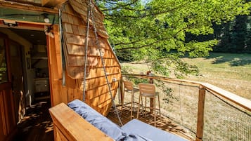 Une cabane en bois dotée d’un balcon, d’un banc et d’une table avec des chaises.