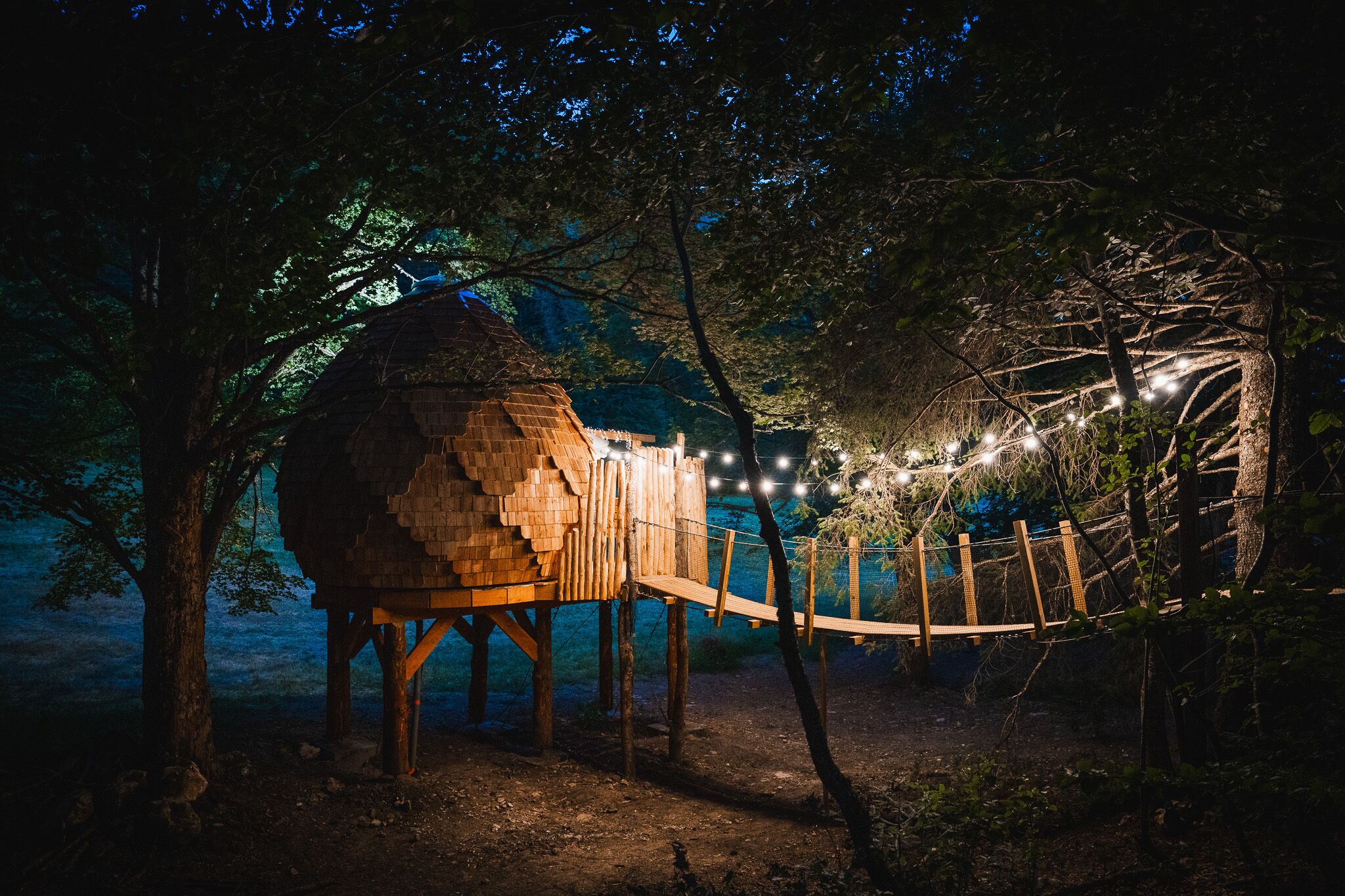 A treehouse with a wooden structure, surrounded by trees and a rope bridge.