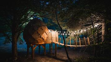 A treehouse with a wooden structure, surrounded by trees and a rope bridge.